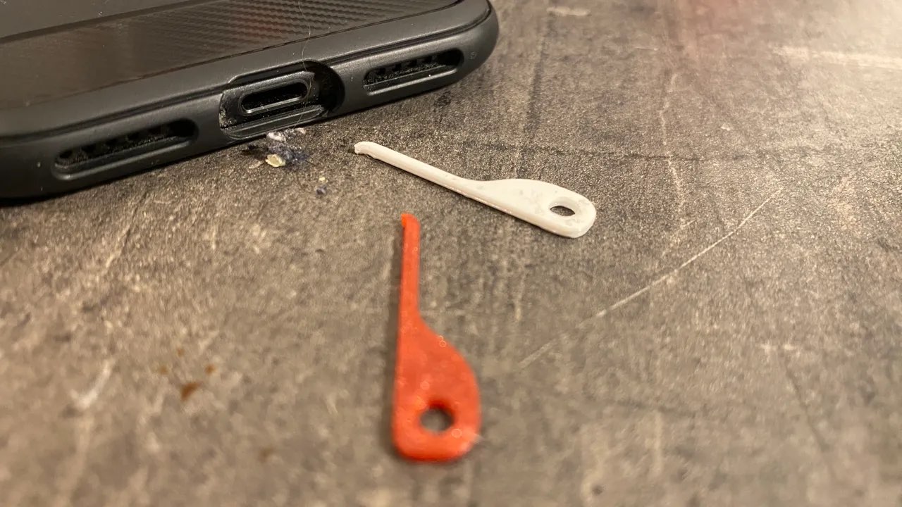 Aus einer USB-C-Ladebuchse herausgeholter Fusselklumpen liegt neben dem Gerät, daneben zwei Werkzeuge aus Kunststoff